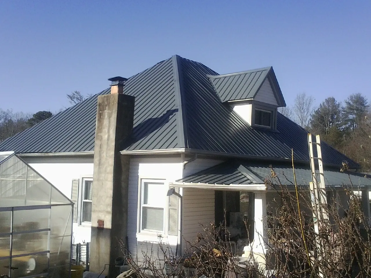 Dark blue standing seam metal roof on a white farmhouse with dormer — Slate & Tile Roof Repair by Roofing Brothers in Pontiac
