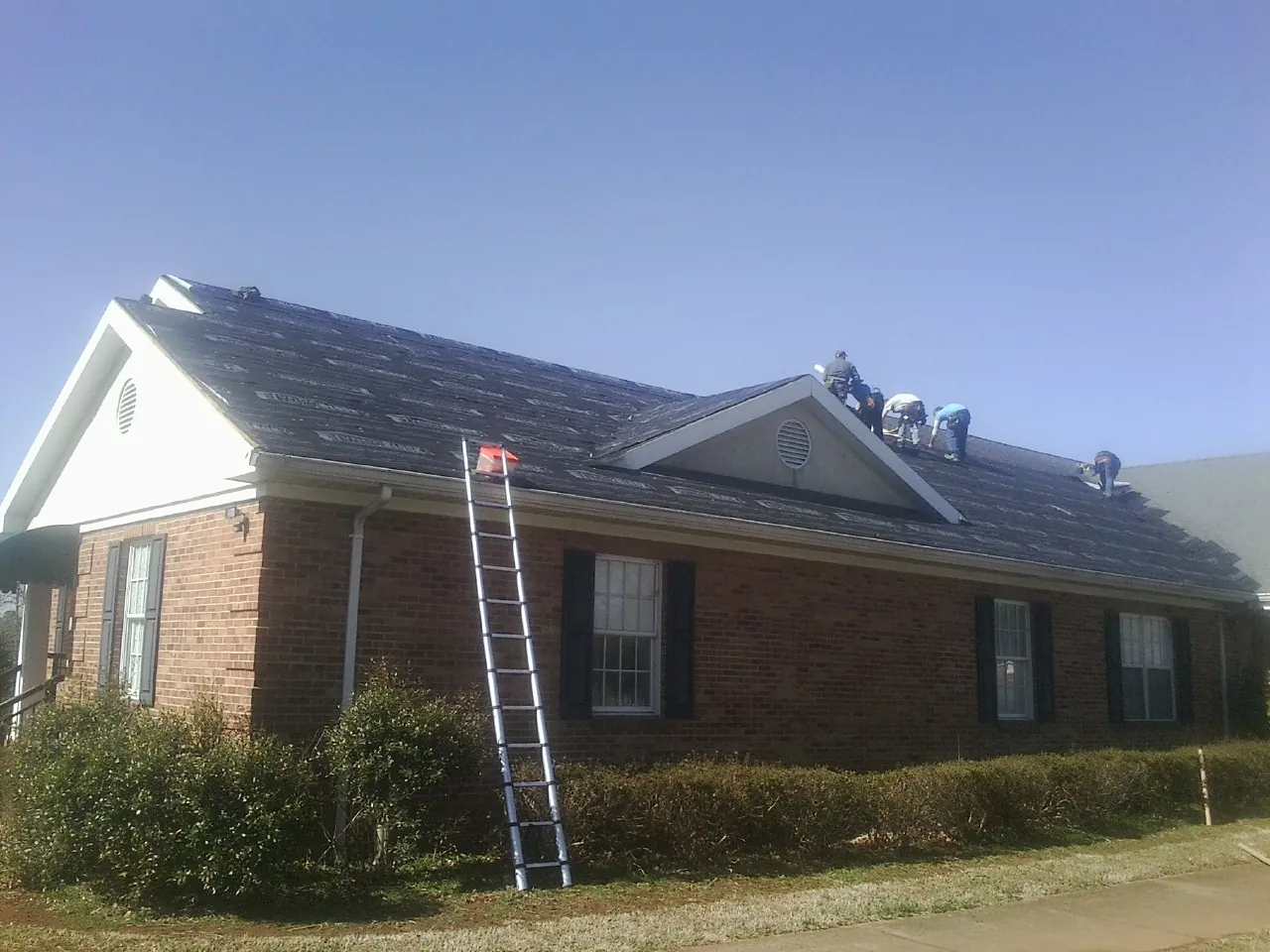 Crew tearing shingles off a brick ranch roof with a ladder set — Emergency Roof Repair work by our crew in Pontiac
