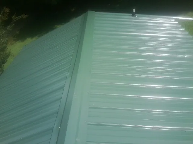 New green metal panels meeting at the ridge of a roof — Flat Roof Repair work by our crew in Pontiac