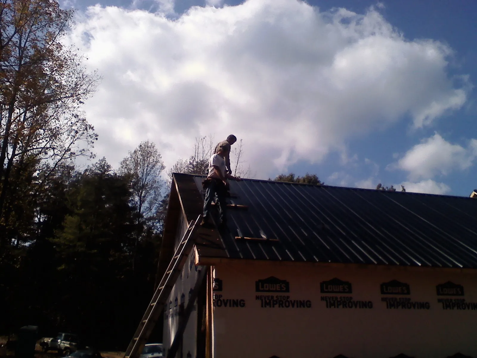 Roofer fastening dark metal panels high against a cloudy sky, from a Roof Inspection job in Pontiac