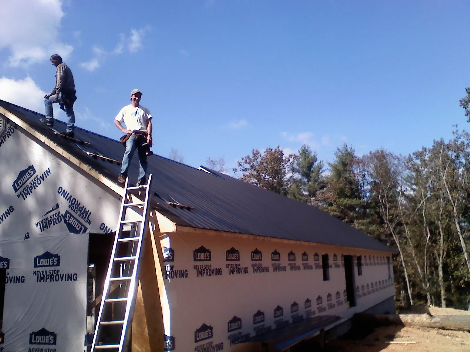 Two roofers standing on a long dark metal roof over a wrapped building in Pontiac