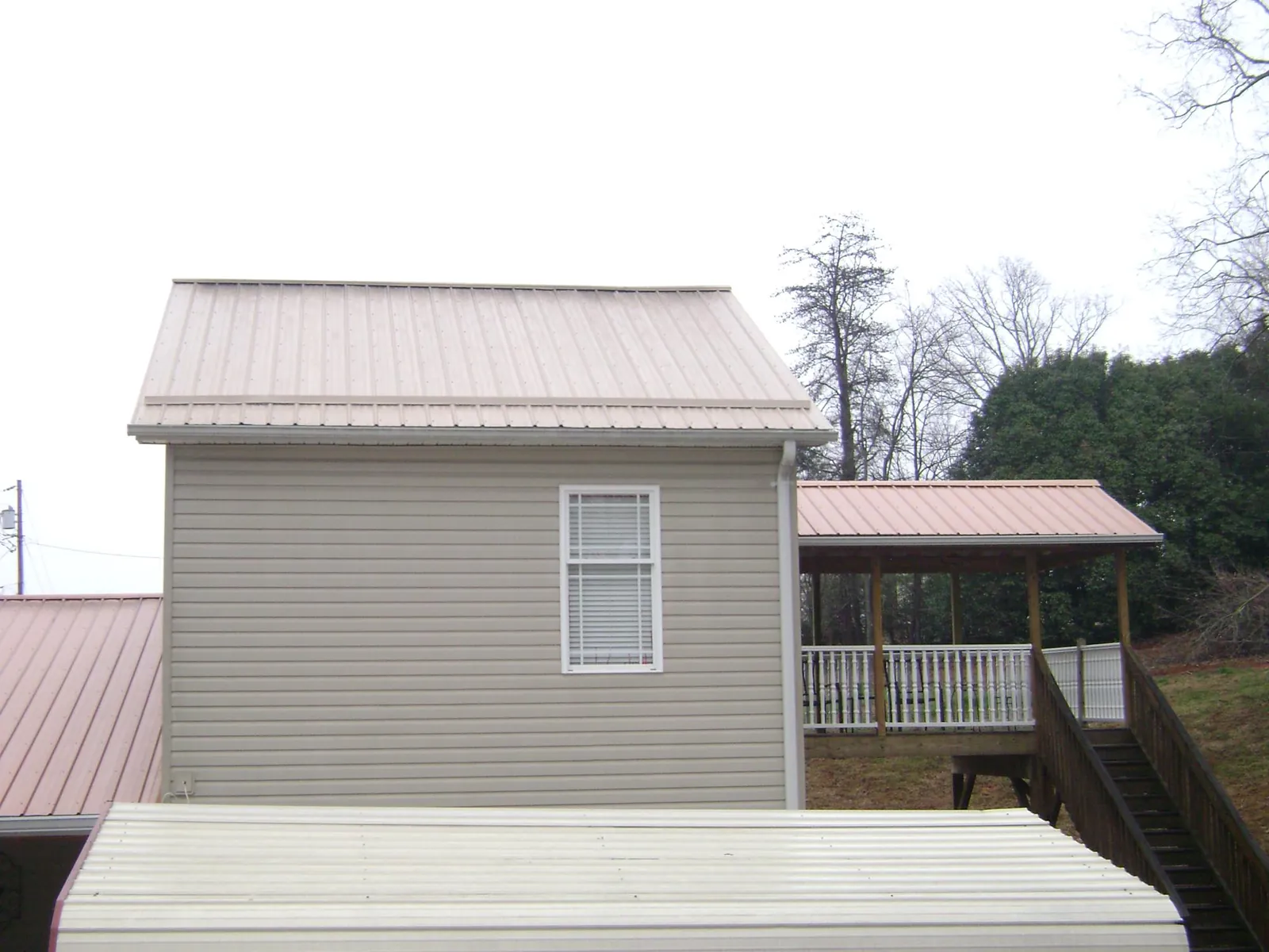 Tan metal roofs on a two story addition and attached porch, from a Roof Replacement job in Pontiac